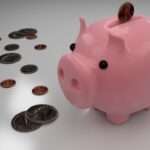 What to know about taxes when buying and selling real estate | taxgirl Pink piggy bank on a reflective surface with coins scattered nearby representing saving money