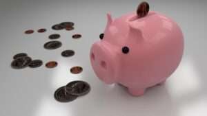 Pink piggy bank on a reflective surface with coins scattered nearby representing saving money