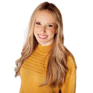 Smiling woman with long blonde hair wearing a mustard knit sweater against a white background facing slightly to the left